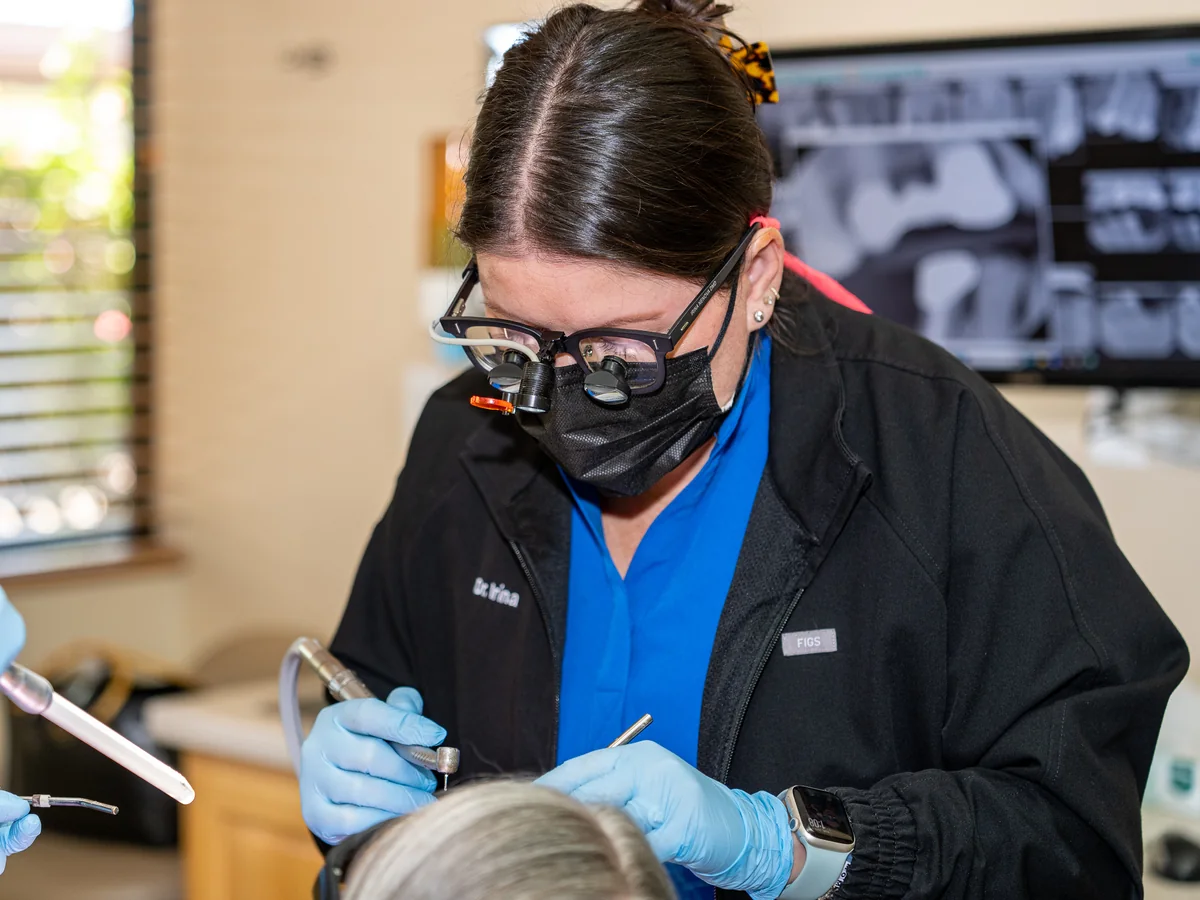 A dentist working under magnification, with the patient's X-rays on screen