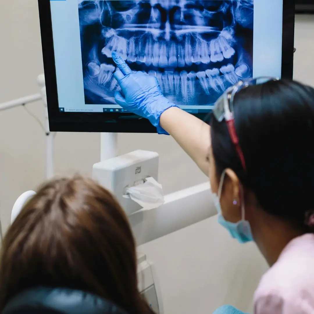 A clinician pointing to a panoramic X-ray on a screen while a patient looks on